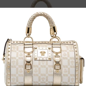 Vit och guld handväska från Versace - Säljer en lyxig handväska från Versace i vitt och guld med ikoniskt mönster och Medusa-detaljer. Väskan har flätade handtag, guldfärgade metalldetaljer och nitar längs kanterna. Tillverkad i skinn och polyester med dragkedja upptill. Perfekt för dig som vill sticka ut.