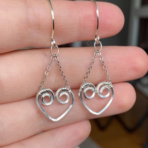 Silvriga örhängen med hjärtform - Unika silvriga örhängen med hjärtformade hängen och spiraldesign. Hängande modell med tunn kedja som ger en lätt och luftig känsla. Perfekta för dig som gillar smycken med en romantisk och kreativ touch.