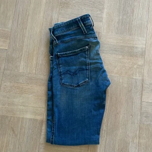 Replay blå slim jeans herr - Snygga blå jeans från Replay med klassisk femficksdesign och diskreta slitningar. Jeansen har smal passform och raka ben, med tydliga Replay-detaljer på fickorna. Perfekta för dig som gillar en stilren och modern look.