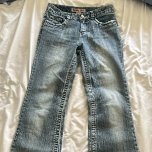 Bonny girl bootcut jeans med paljetter - Säljer ett par ljusblå bootcut jeans från Bonny girl med snygg slitning och paljettbroderi på bakfickorna. De är uppsprättade längst ner på benen för att göra dem längre. Klassisk femficksmodell med låg midja och coolt bling-detalj baktill. Perfekta för dig som vill sticka ut lite extra.