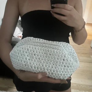 Handgjord vit stickad handväska - Superfin handgjord handväska i chunky stickat material. Väskan är vit och har en mjuk, rektangulär form med kllasp. 