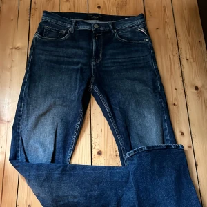 Blå jeans från Replay, modell Thad - Snygga blå jeans från Replay i klassisk femficksmodell. Jeansen har en mörk tvätt med lätt slitning och raka ben. Märkespatch bak i midjan och diskreta detaljer. Perfekta för dig som gillar en tidlös och stilren look.