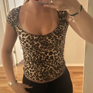 Leopardmönstrad topp från Nelly - Säljer en snygg leopardmönstrad topp från Nelly i storlek S. Toppen har korta ärmar, djup rundad urringning och figurnära passform. Färgerna går i beige och brunt med svarta detaljer. Säljs då den inte kommit till användning