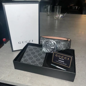 Gucci GG Supreme bälte med silverdetalj - Säljer ett Gucci GG Supreme bälte i svart och grått med klassiskt GG-mönster och stor silverfärgad GG-spänne. Bältet är gjort i skinn med tryckt canvas på utsidan och ljus insida. Perfekt för dig som vill ha en lyxig och trendig accessoar.