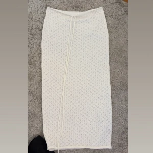 Vit långkjol med snörning - Snygg vit långkjol med diskret rutmönster och snörning framtill. Kjolen har en rak passform och är perfekt för dig som gillar stilrena och trendiga plagg. Enkel att matcha med både sneakers och sandaler.