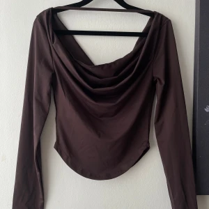 Brun långärmad topp med draperad urringning - Säljer en brun långärmad topp med snygg draperad urringning både fram och bak. Toppen har en tight passform och stretchigt material. 