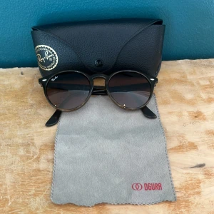 Ray-Ban runda solglasögon brun - Snygga runda Ray-Ban solglasögon i brun transparent plast med mörka linser. Modellen är RB2180-F och de har klassisk Ray-Ban-logga på linsen. Kommer med svart Ray-Ban-fodral och putsduk. Perfekta för att lyfta din stil i solen.