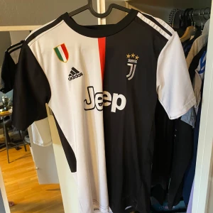 Juventus Ronaldo 7 matchtröja Adidas - Juventus officiella matchtröja med Ronaldo 7 på ryggen. Tröjan är svart och vit med en röd rand i mitten, kortärmad och tillverkad i lätt och ventilerande material. Adidas-logga, Juventus klubbmärke och Jeep-sponsor på framsidan.
