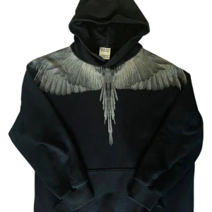 Marcelo Burlon hoodie - Svart hoodie från Marcelo Burlon County of Milan med ikoniskt vingtryck i grå toner över axlar och bröst, samt på ryggen. Tröjan har huva, känguruficka och är tillverkad i mjuk bomull. Perfekt för dig som vill sticka ut med streetwear vibes.