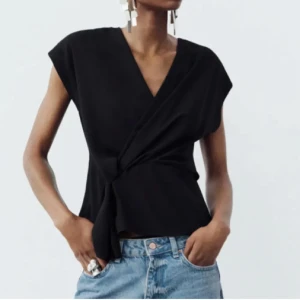 Svart omlottopp från Zara - Svart omlottopp från Zara med snygg v-ringning och knyt i sidan. Toppen är ärmlös och har en stilren, lite lös passform som ger en cool och avslappnad vibe. Perfekt att matcha med jeans eller kjol för en trendig look. storlek xs men passar även s.