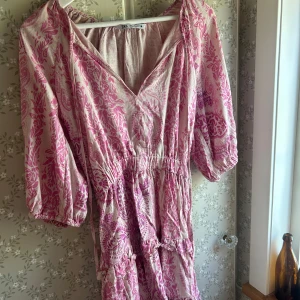 Rosa mönstrad kortklänning från Zara - Superfin kortklänning från Zara i ljusrosa med mönster i starkare rosa. Klänningen har v-ringning med knyt, resår i midjan och trekvartsärmar med resår. Tillverkad i ett tunt och luftigt material, perfekt för varma dagar.