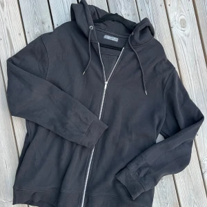 Svart hoodie med dragkedja Primark 3XL - Svart hoodie från Primark i storlek 3XL. Tröjan har hel dragkedja framtill, huva med snörning och långa ärmar. Tillverkad i mjuk bomullsmix, perfekt för chill dagar. Enkel och stilren design utan mönster eller tryck.