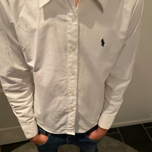 Vit skjorta från Polo Ralph Lauren  - Klassisk vit skjorta från Polo Ralph Lauren står l men skjortan passar xs den är figursydd Skjortan har lång ärm, knappar framtill och den ikoniska broderade loggan på bröstet. Tillverkad i mjuk bomull och passar perfekt till jeans eller chinos.