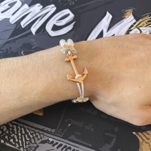 Armband - Snyggt armband med ett guldigt ankare som lås och tjockt, tvinnat vitt rep. Perfekt accessoar för dig som gillar marina vibes och stilrena detaljer. Ankaret ger en cool touch och armbandet är lätt att justera efter handleden.