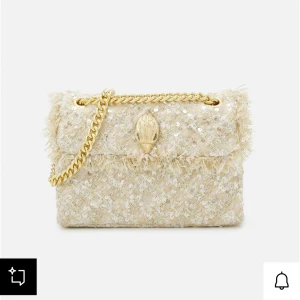 Kurt geiger väska - Superfin beige axelväska från Kurt geiger med glittriga paljetter, fransiga kanter och guldfärgad kedja. Väskan har ett snyggt fågelspänne framtill och är gjord i ett tweedliknande tyg. Perfekt för dig som vill sticka ut med en lyxig och trendig accessoar.