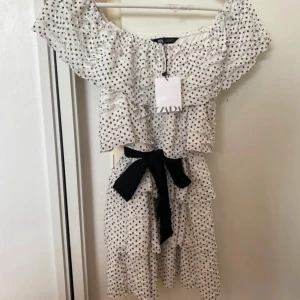 Prickig offshoulder klänning från Zara - Superfin och populär off shoulder klänning med volanger ifrån Zara tillsammans med ett svart knytband , aldrig använd med prislapp kvar därav inga defekter och som ny! 