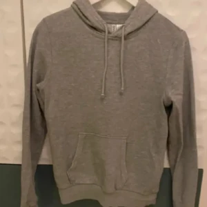 Grå Hoodie från H&M! -  Endast använd vid 1 tillfälle! Enkel och stilren grå hoodie med huva och dragsnören. Tröjan har en stor magficka framtill och ribbade muddar vid ärmslut och nederkant. 