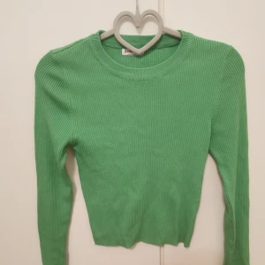 Grön ribbad långärmad tröja - Snygg grön ribbad tröja från Stradivarius med lång ärm och rund hals. Modellen är figurnära och croppad, perfekt att styla med höga jeans eller kjol. Enkel men trendig look som passar året runt.