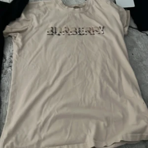 Beige Burberry t-shirt med logga - Snygg beige t-shirt från Burberry med klassisk logga i mönstrad stil över bröstet. T-shirten har rund halsringning och korta ärmar. Perfekt för dig som gillar stilrena och exklusiva plagg med en twist.