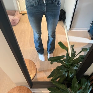 Lågmidjade jeans - Säljer ett par blå bootcut jeans från H&M med låg midja och justerbar midja. Jeansen har klassisk femficksdesign, snygga bakfickor med lock och knappar samt en lätt tvättad look. Perfekta inför höst/vinter/vår. 