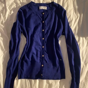 Marinblå kofta från Holly & Whyte XS - Snygg marinblå kofta från Holly & Whyte i storlek XS. Koftan har guldiga knappar framtill, rund halsringning och är ribbad vid ärmslut och nederkant. Endast 2 gånger använt, inga defekter. 