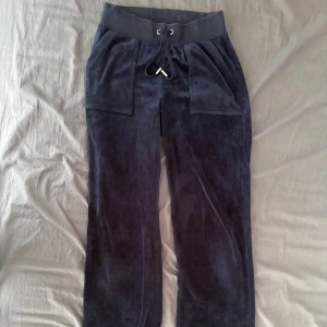 Marinblå velourbyxor Juicy Couture XXS - Marinblå mjukisbyxor från Juicy Couture i mjuk velour. Byxorna har bred resår i midjan med snörning, stora fickor fram och bakfickor med knappar. Klassisk relaxed passform och riktigt skön känsla.