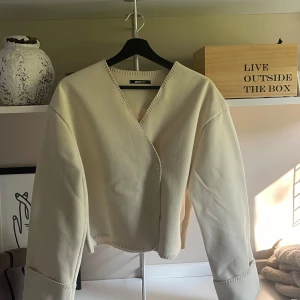 Beige omlottkofta från Gina Tricot - Säljer en beige omlottkofta från Gina Tricot i storlek S. Koftan har lång ärm, markerade sömmar och en snygg omlott-skärning framtill. Perfekt för lager-på-lager och enkel att styla med dina favoritjeans eller kjol.