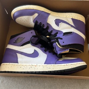 Nike Air Jordan 1 High Lila/Vit - Nike Air Jordan 1 High i lila och vitt med svarta skosnören och detaljer. Ovandel i kombinerat skinn och textil, klassisk Jordan-logga på sidan och Zoom Air-märke på plösen. Sulan är vit med färgade prickar och svart yttersula.  Skorna är enbart testade och är i nyskick. Kvitto finns även om så önskas! skorna kostade 1700 nya men har stigit i pris så detta är en dunder deal!