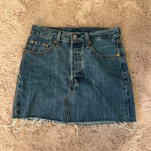 Jeanskjol - Säljer en klassisk blå jeanskjol från Levi's som är fransig. Kjolen har normal passform och tydliga sömmar, samt Levi's ikoniska läderpatch och röda etikett bak. Perfekt för dig som gillar en avslappnad och cool stil. I storlek 26😇