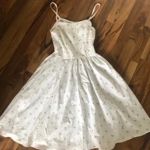 Vit blommig sommarklänning med smala axelband - Superfin vit klänning med små blommor i beige, smala axelband och utsvängd kjol. Lätt och luftig bomull, perfekt för varma dagar. Söt och enkel design med diskret blommönster över hela klänningen. Knäppes med blixtlås i sidan. Passar Xs. Säljes då den blev för liten för mig.☀️ 50tals stil✨