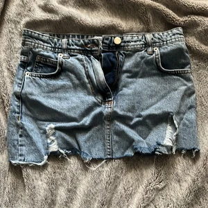Blå jeanskjol från Madlady XS - Säljer en blå jeanskjol från Madlady i storlek XS. Kjolen är kort, har slitna detaljer och fransig nederkant för en cool vibe. Klassisk femficksmodell med dragkedja och knapp framtill. Perfekt till boots. 