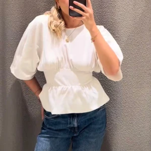 Vit blus med puffärm och öppen rygg - Superfin vit blus med puffiga korta ärmar och markerad midja. Baksidan har öppen rygg och en stor knytrosett som ger en snygg detalj. Aldrig använd 