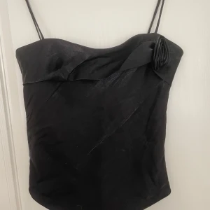 Svart linne med en rosdetalj - Snyggt svart linne med tunna axelband och en rosdetalj framtill.