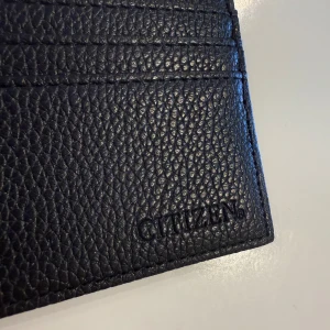 Svart korthållare - Minimalistisk svart korthållare från Citizen i präglat skinn. Den har flera kortfack och en stilren design som passar perfekt i fickan. Perfekt för dig som vill ha koll på korten utan att bära runt på en stor plånbok. Ord pris 299kr. 