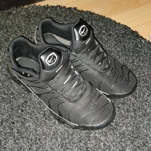 Nike Air Max Plus TN  - Nike Air Max Plus TN sneakers i helsvart med diskreta vågmönster och mesh-överdel. Snygga detaljer som TN-logga bak och synlig Air Max-dämpning i sulan. Hyfsat använda lite småskador men inget stort. 