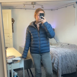 Mörkblå dunjacka från Colmar - Säljer en mörkblå dunjacka från Colmar med klassisk pufferdesign. Jackan har dragkedja framtill, två fickor med dragkedja och hög krage. Perfekt för kyliga dagar och riktigt snygg till jeans eller mjukisbyxor. Tyvärr har Colmar märket gått av på baksida av jackan