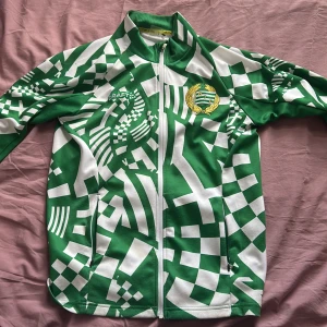 Grönvit Craft Hammarby tröja - Säljer en grön och vit tröja från Craft med Hammarby IF-emblem broderat på bröstet. Jackan har ett unikt grafiskt mönster, hel dragkedja och lång ärm. Perfekt för dig som vill sticka ut på läktaren eller i vardagen.