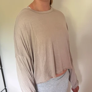 Beige croppad långärmad tröja - Säljer en beige croppad långärmad tröja med loose passform. Tröjan har rund halsringning och är tillverkad i ett tunt, mjukt material som känns skönt mot huden. Perfekt för en avslappnad och chill stil.