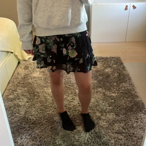 Blommig volangkjol från KappAhl - Supersöt svart kortkjol från KappAhl med blommigt mönster i grönt, rosa och vitt. Kjolen har volanger och resår i midjan för en skön passform. Storlek 134/140 men skulle säga att den passar som XS, lite lite liten på mig som är 165. Pris kan diskuteras!