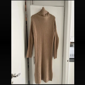   stickad långklänning - Supermysig beige stickad långklänning med polokrage och långa ärmar. Klänningen har en ribbad struktur som ger en snygg och trendig look. Perfekt för kyliga dagar när du vill vara både bekväm och stilren.