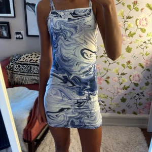 Blåvitt kläning - Supersnygg kortklänning med blåvitt swirl-mönster och smala axelband. Tight passform som framhäver figuren och ger en modern vibe. Perfekt för dig som vill sticka ut med ett unikt print. Materialet känns mjukt och följsamt mot kroppen. Passar en xxs