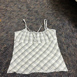 Rutig linnetopp med knytband - Supersöt rutig linnetopp i vitt och grått med tunna axelband som knyts upptill. Dragkedja i sidan. Lapp bortklippt men uppskattas till xs-s. 🩷