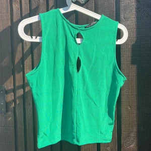 Grön ärmlös topp med cut outs - Snygg grön ärmlös topp cut outs fram och bak Modellen är croppad och har en enkel, stilren design som passar perfekt till jeans eller kjol. Materialet känns mjukt och stretchigt, vilket gör den bekväm att bära hela dagen.