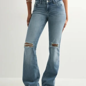 Ljusblå bootcut jeans med slitningar - Snygga ljusblå jeans med bootcut passform och slitna detaljer vid knäna. Jeansen har klassisk femficksdesign och coola broderade detaljer på bakfickorna. Perfekta för en avslappnad och trendig look.