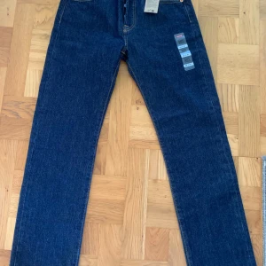 Levi's 501 mörkblå jeans 28/30 - Klassiska Levi's 501 jeans i mörkblå denim med raka ben och hög midja. Snygga kontrastsömmar, fem fickor och ikonisk röd Levi's-tag på bakfickan. Perfekta för dig som gillar tidlös stil och vill ha ett par jeans som alltid funkar. Och den är helt oanvända och helt nya kom med pris förslag 