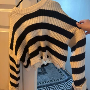  tröja från Bershka - Säljer en ribbstickad croppad tröja från Bershka i svart och vitt. Tröjan har breda ränder, lång ärm och råa kanter nertill för en edgy look. Perfekt för dig som gillar streetstyle och vill sticka ut lite extra.