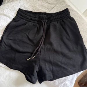 Svarta shorts med snörning H&M XS - Svarta mjuka shorts från H&M Basics i storlek XS. De har elastisk midja med snörning och är tillverkade i bomull och polyester. Perfekta för chill dagar eller träning, med enkel och clean look.