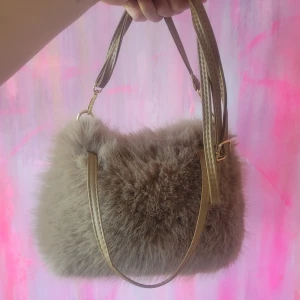 Beige fluffig axelväska med päls - Supermjuk och fluffig beige axelväska med lång justerbar rem i läderimitation och guldfärgade detaljer. Väskan har en rektangulär form och är täckt av pälsmaterial som ger en mysig och trendig look. Perfekt för dig som vill sticka ut med en unik accessoar. Så sjukt snygg och påminner om den sjukt populära på sista bilden!🩷🩷 så snygg men har för mycket väskor så måste sortera ut de jag inte använder! Kika gärna på mina andra annonser 🩷💖 aldrig använd!