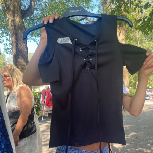 Svart snörad topp  - Svart kortärmad topp med cool snörning framtill. Toppen har cut out-detaljer vid axlarna och är gjord i ett ribbat material som ger en snygg struktur. Perfekt för dig som vill ha en edgy och trendig look.