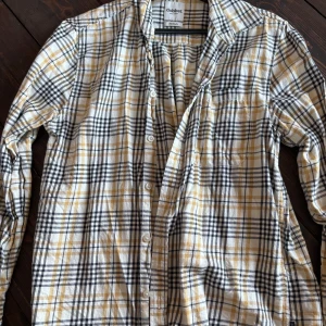 Rutig skjorta från Dobber i bomull - Riktigt snygg rutig skjorta från Dobber i vitt, svart och beige med inslag av gult. Skjortan har klassisk krage, långa ärmar och knäppning framtill. Perfekt för dig som gillar en avslappnad men ändå stilren look.